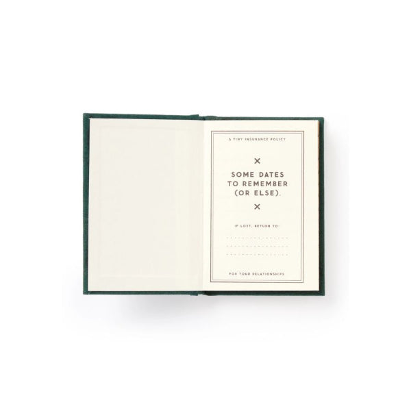 An open notebook or journal with a dark green cover and cream-colored pages, featuring a minimalist printed card on the right page with the text 'SOME DATES TO REMEMBER (OR ELSE)'.