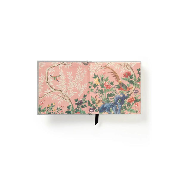 A hardcover notebook with an ornate floral and bird pattern on a dusty pink cover, shown open against a plain white background.