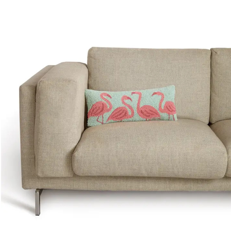 Beige sofa with a decorative pillow featuring pink flamingos on a white background