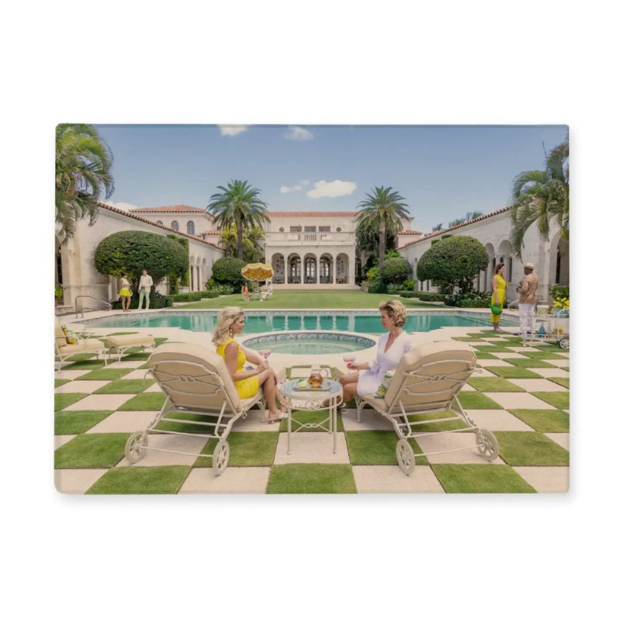 Two women sitting on lounge chairs by a pool in a luxurious garden setting.