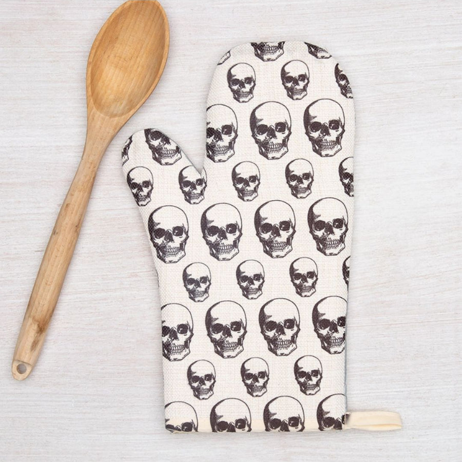 Oven mitt with skull pattern next to a wooden spoon on a light background